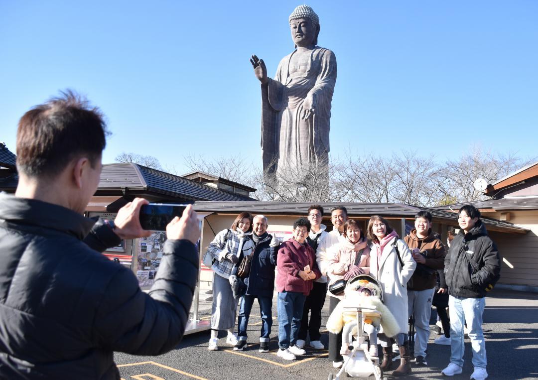 牛久大仏を背景に記念写真を撮る、マレーシアからの観光客=牛久市久野町