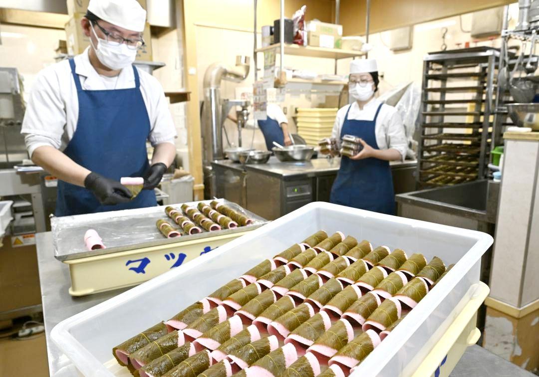 桜の葉を丁寧に巻き、桜餅を仕上げる従業員=行方市山田