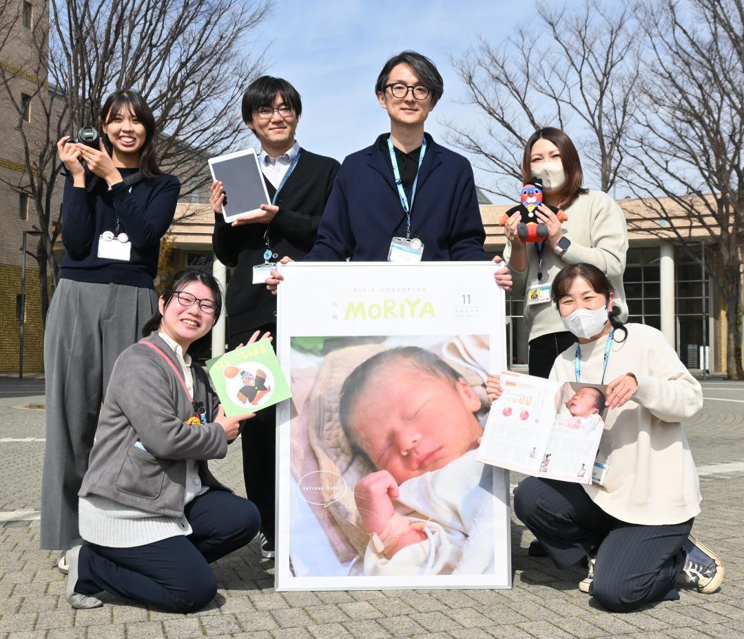 特選を受賞した広報紙のパネルなどを手にする職員ら=守谷市役所